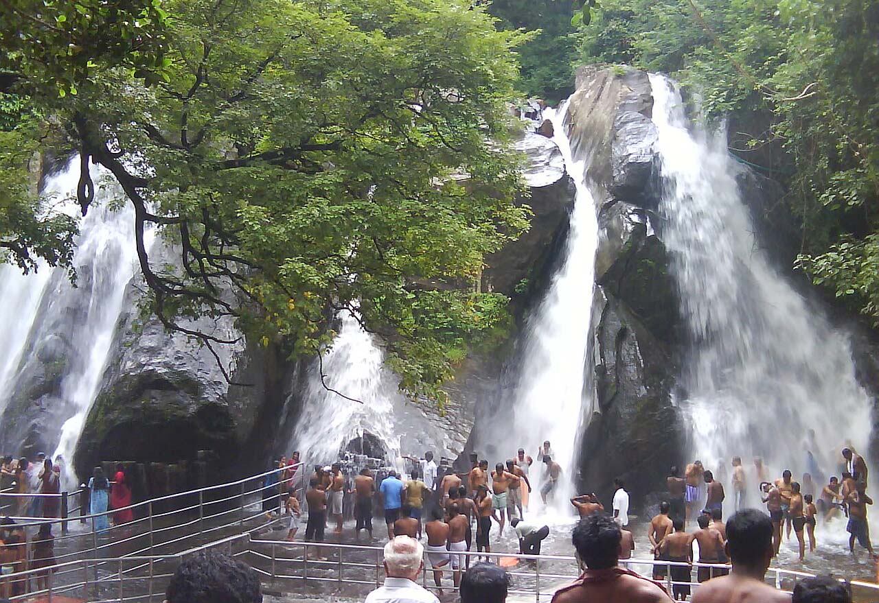 Courtallam Five Falls with people bathing, waterfalls, and green trees in Tamil Nadu, India.